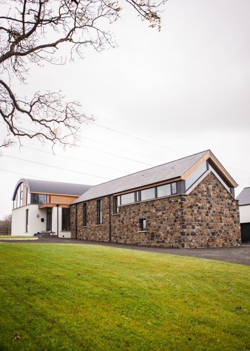 Wider shot of home with pitched field stone barn and corrugated metal clad barrel roof
